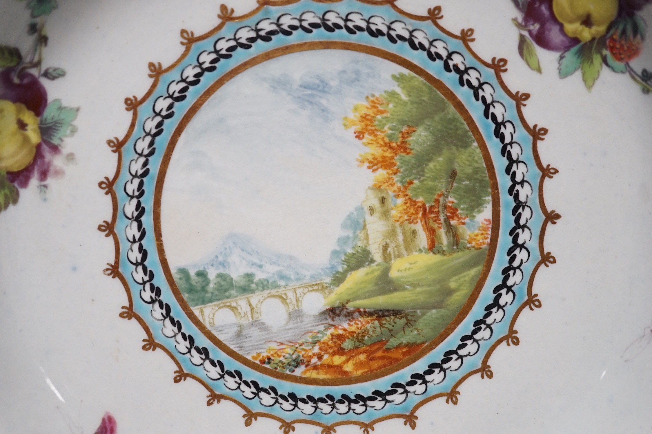 A Worcester plate painted with a landscape surrounded by fruit and moths under a blue and gilt border, in one of the variations of the Lord Dalhousie pattern (over restored chip to reverse only), 21.5 cm